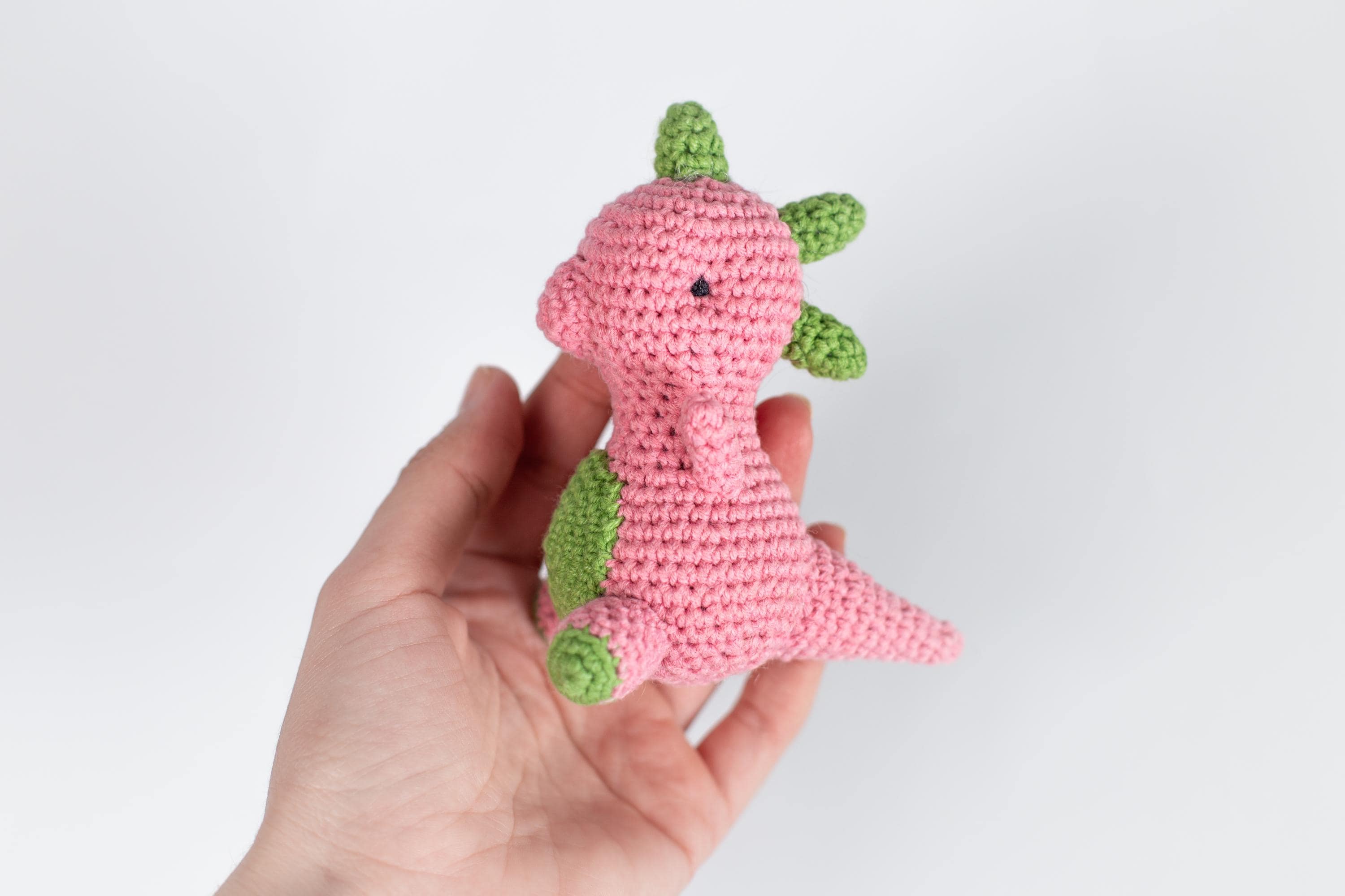 a hand holding a pink crocheted stuffed animal
